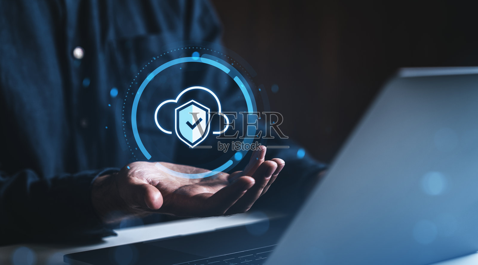 在黑暗背景下，云数据安全图标漂浮在手掌上方，旁边有一台笔记本电脑。照片摄影图片