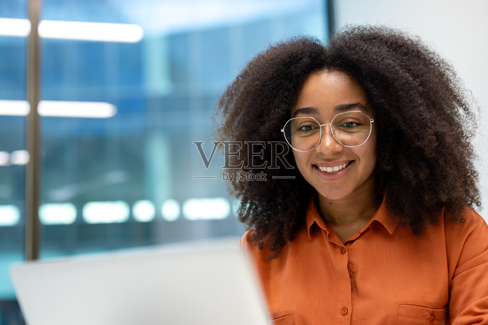 一位戴眼镜的微笑年轻女性在使用笔记本电脑时看向镜头。照片摄影图片