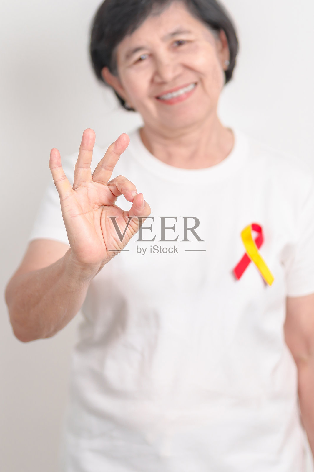 世界肝炎日宣传月，7月28日。老年女性佩戴红色和黄色丝带。肝癌、黄疸、肝硬化、肝功能衰竭、肝脏肿大、肝性脑病和健康概念。照片摄影图片