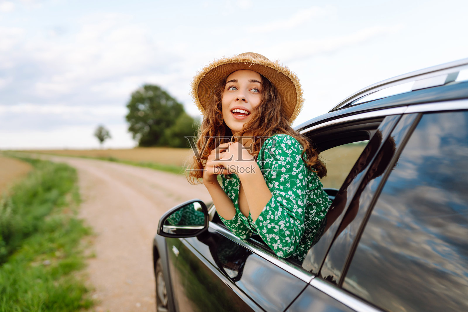 戴着帽子和鲜艳裙子的旅行者倚靠在车窗外。照片摄影图片
