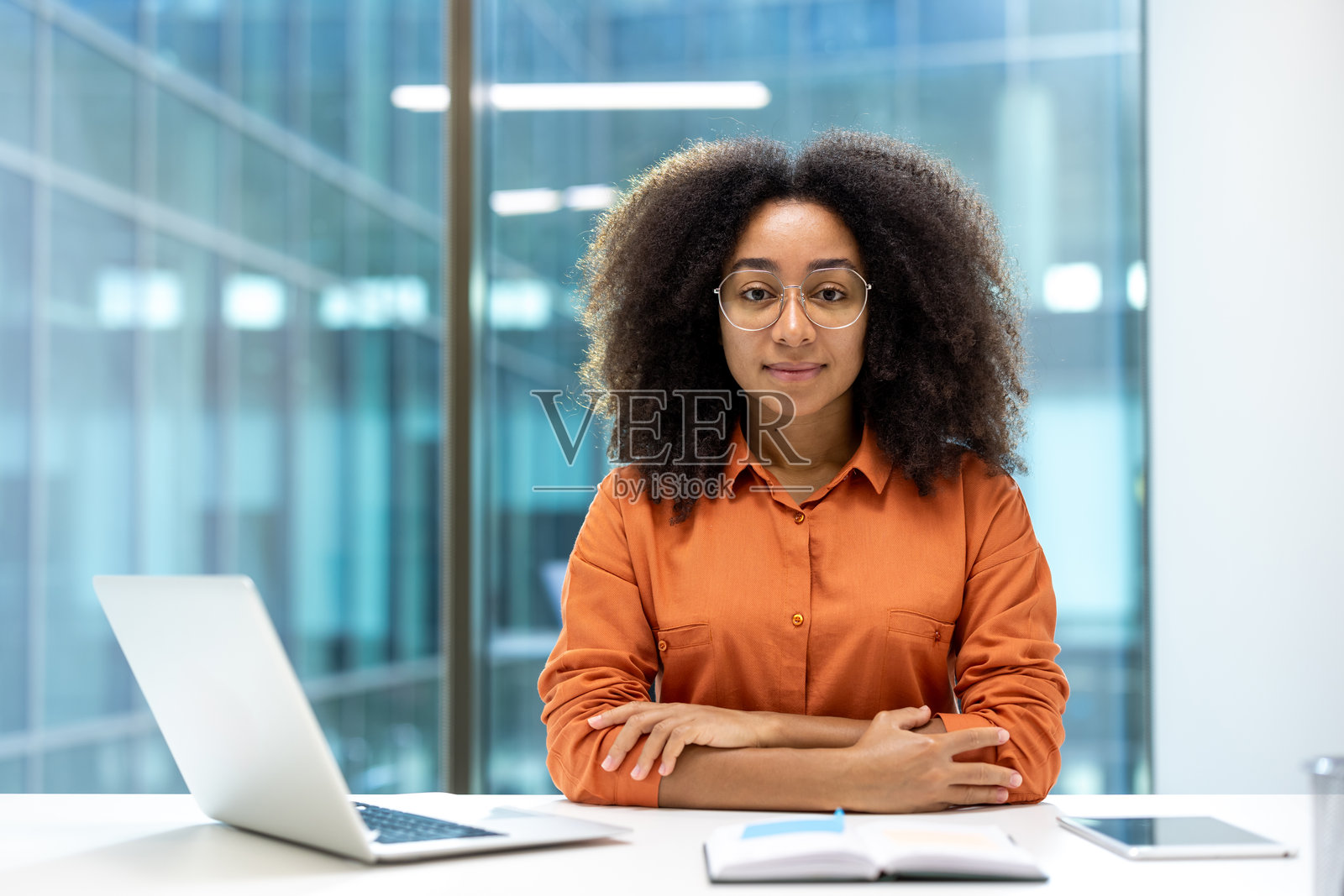 成功女商人在办公室的肖像。她坐在桌子旁，面前有一台笔记本电脑，自信地看着镜头。照片摄影图片