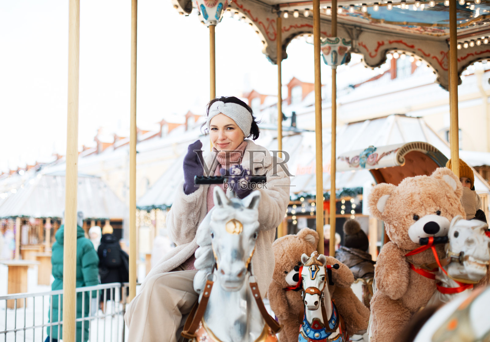 美丽的棕发女性在旋转木马上。模特骑在马背上，在冬季假期中尽情玩乐。照片摄影图片