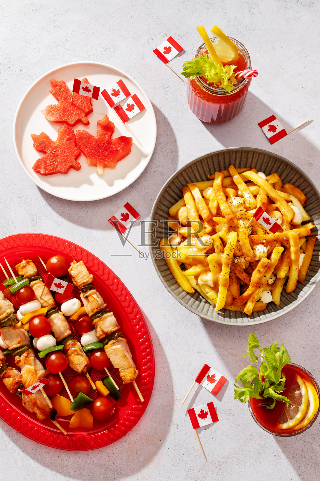 从上方俯视的加拿大国庆派对食物，包括肉汁薯条、热狗、水果、串烧和装饰有加拿大国旗的甜甜圈照片摄影图片