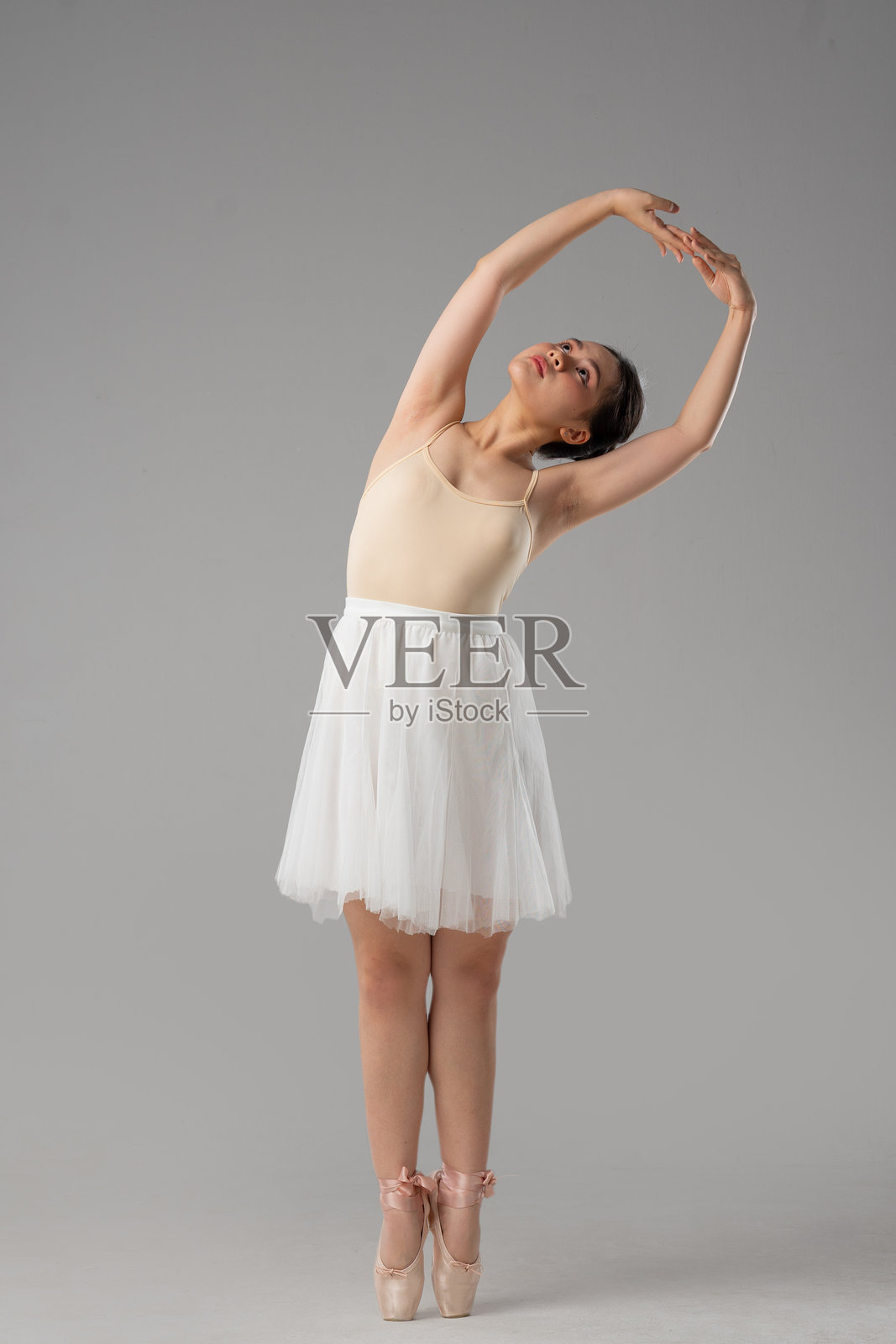 年轻的芭蕾舞者优雅地弯曲身体，双臂高举，处于经典芭蕾舞姿势，仰望着天空。照片摄影图片