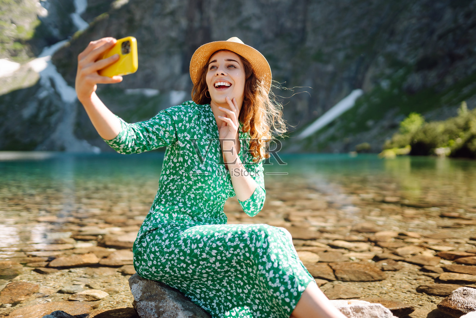 一位开心的女性在山湖背景下用手机自拍。照片摄影图片