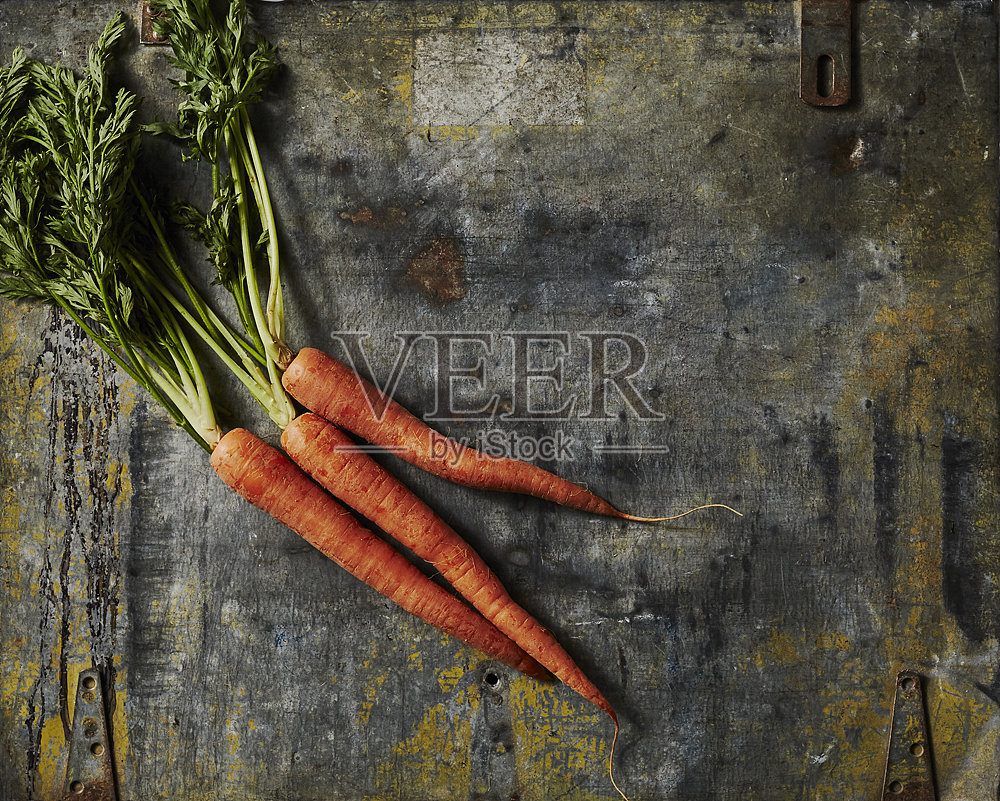 新鲜胡萝卜与绿叶放在磨损的金属表面上照片摄影图片