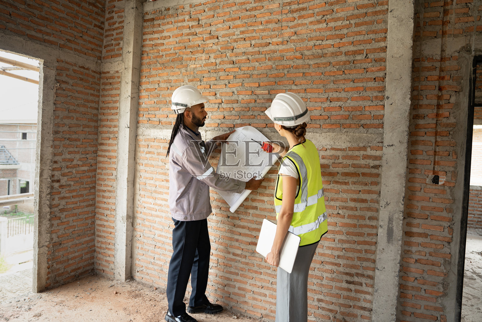 两名工程师在建筑工地上工作。工头使用笔记本电脑和纸质文件。照片摄影图片