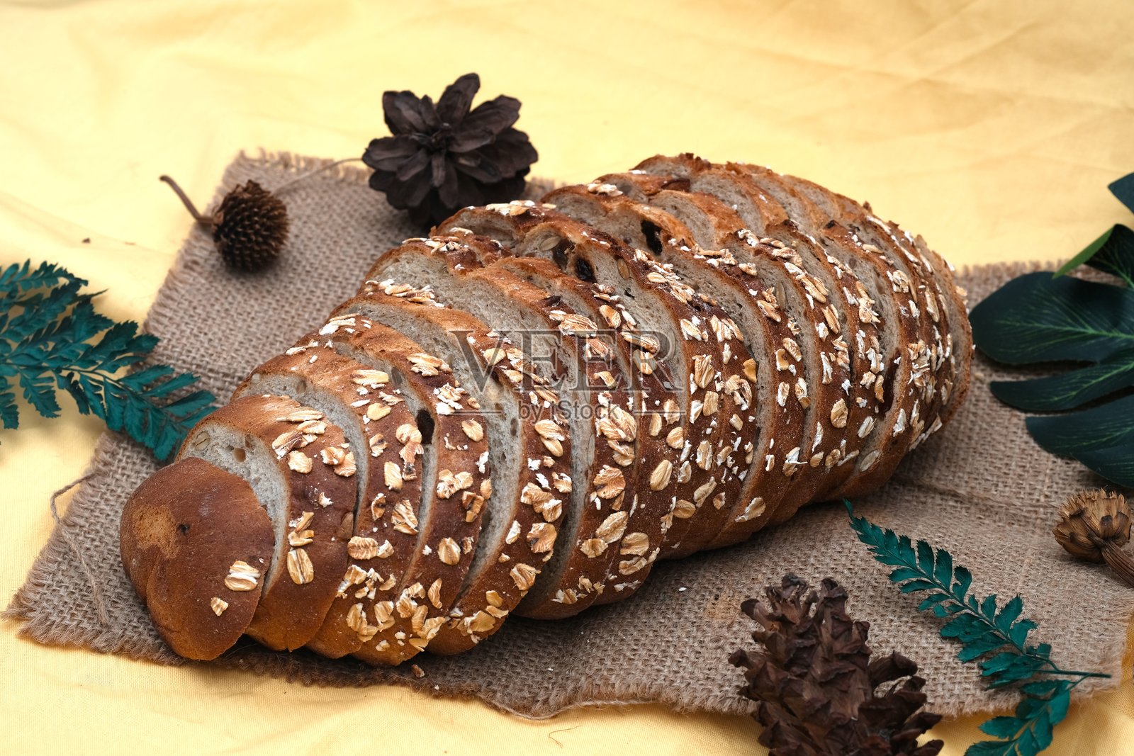 几片多谷物面包静静地放在木盘上，盘子上铺着麻布，周围环绕着松果和小麦等自然装饰。照片摄影图片