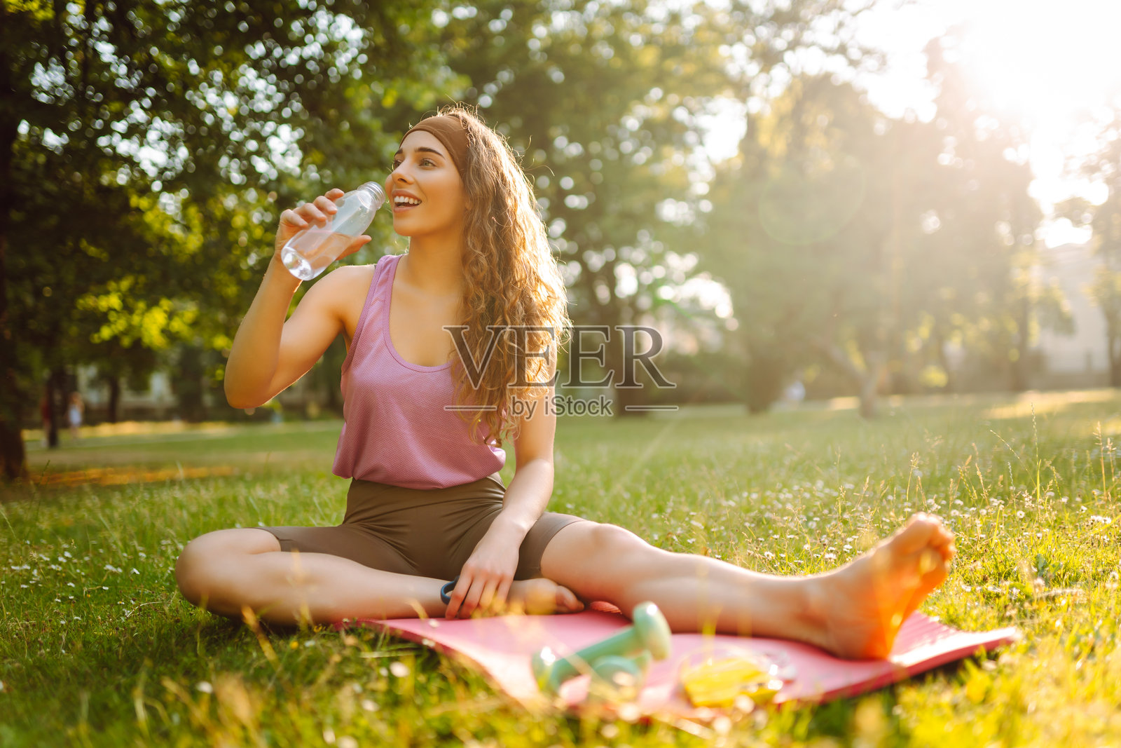 年轻女性穿着运动服在阳光明媚的公园里垫上锻炼。照片摄影图片