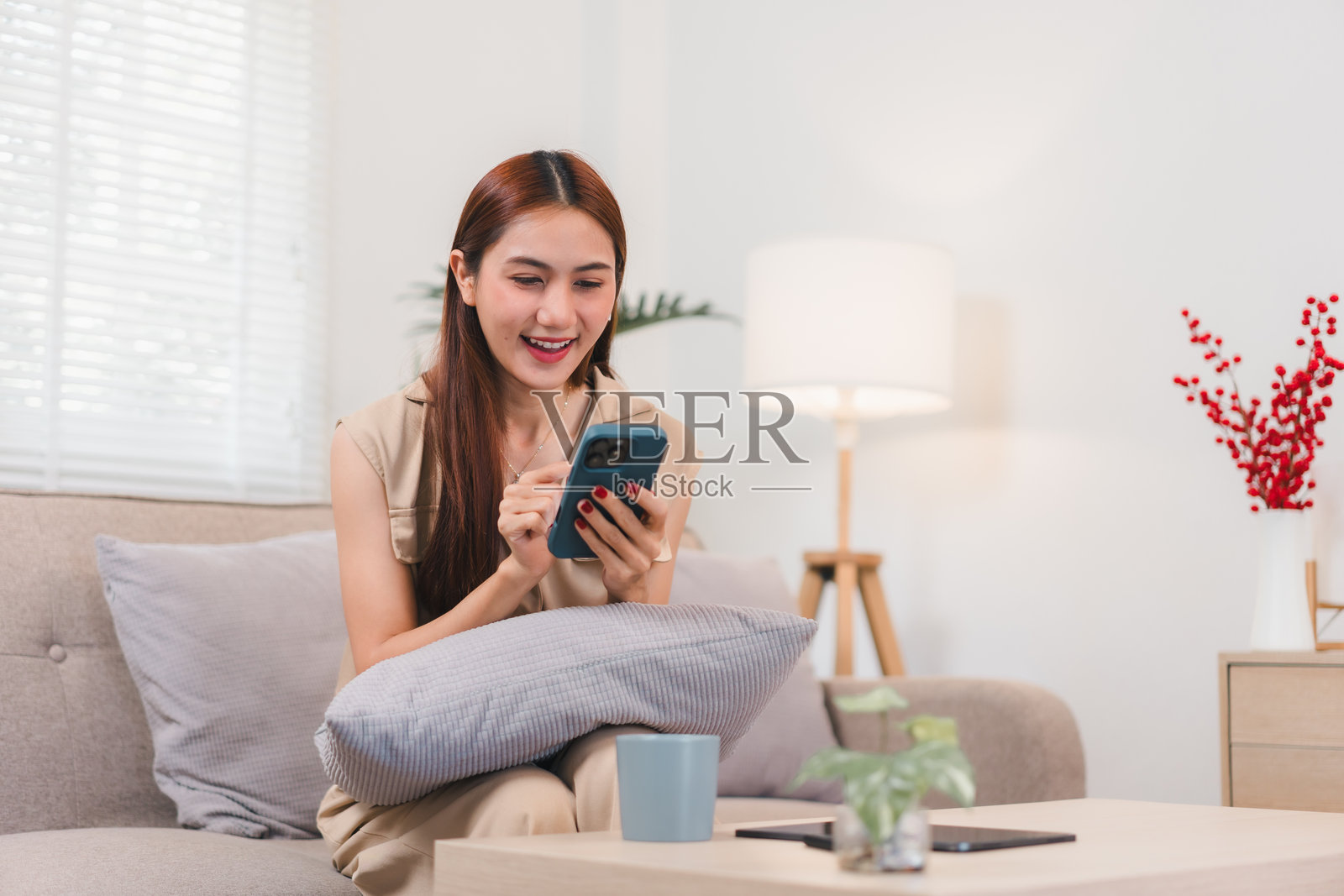 愉快的亚洲女性坐在沙发上，在现代装饰的舒适客厅里使用智能手机。照片摄影图片