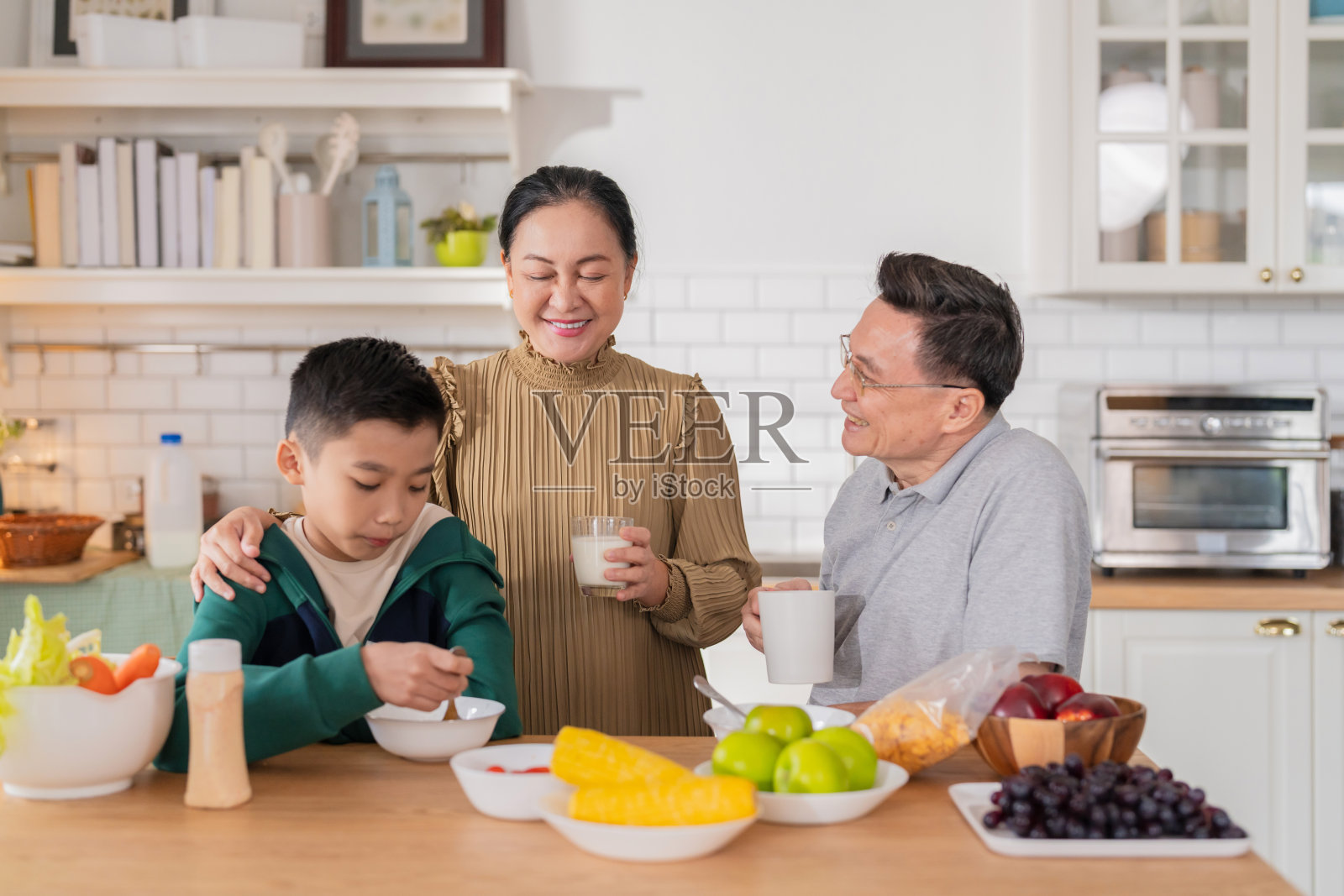 快乐的亚洲家庭分享温馨时刻，祖父母在家中与孙子享受早餐对话。祖母和小男孩在开放式厨房一起洗新鲜水果，创造了愉快的亲密体验。照片摄影图片
