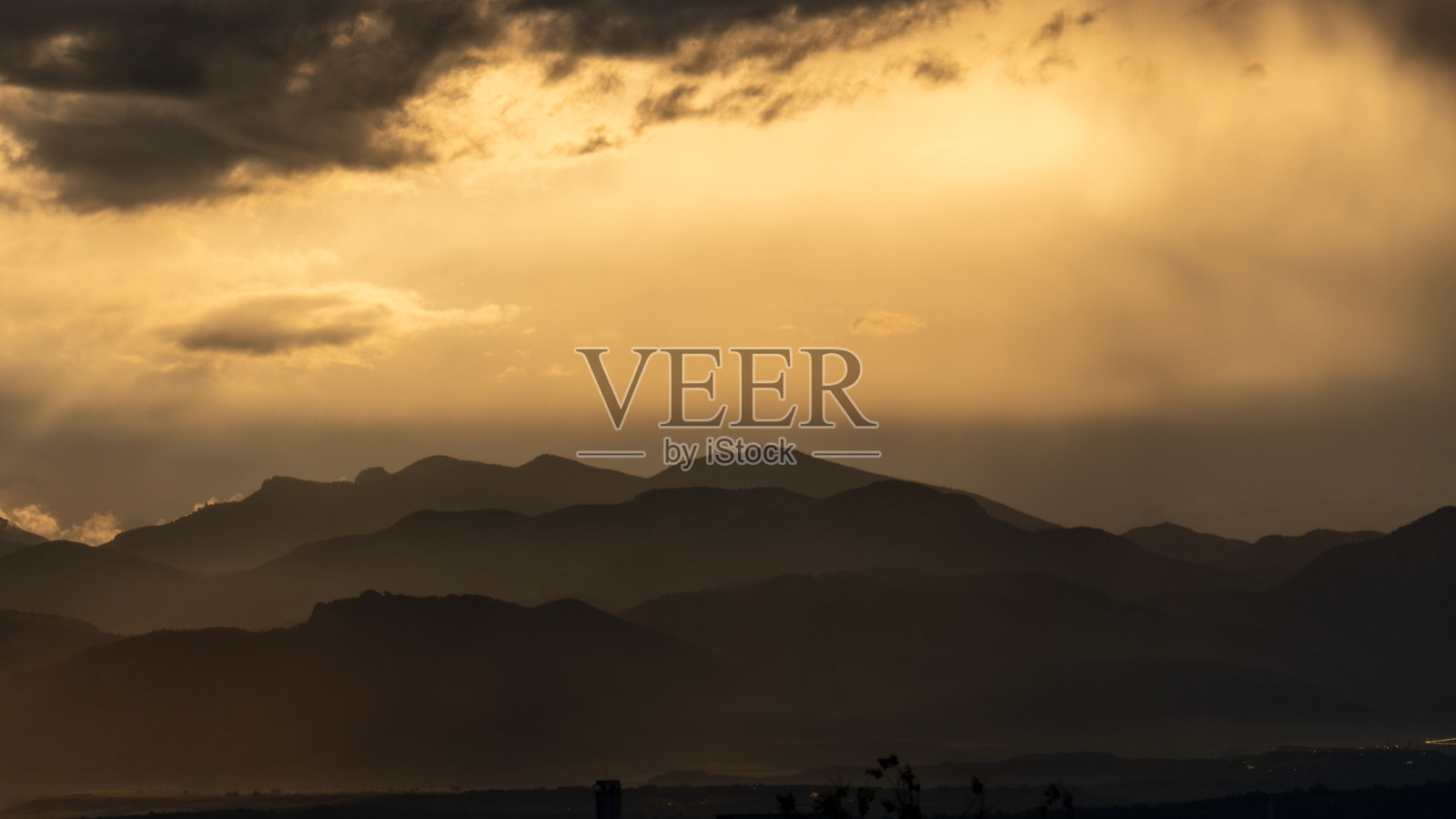 夕阳的光线穿透暴风云。戏剧性的山脉轮廓形成分层的风景。照片摄影图片