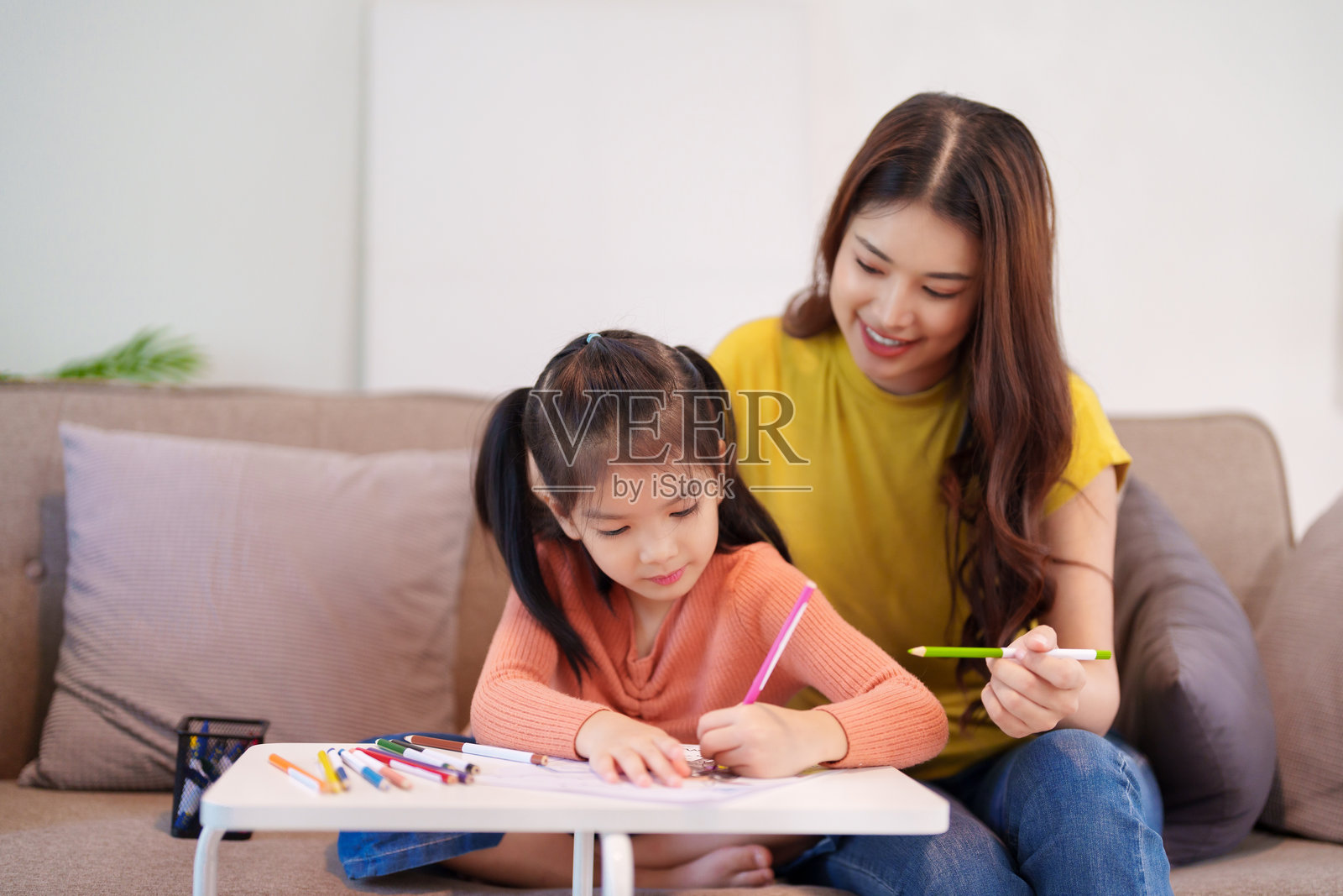 一位母亲在桌子旁帮助女儿做作业，周围是书籍和文具，营造出学习和支持的氛围。照片摄影图片