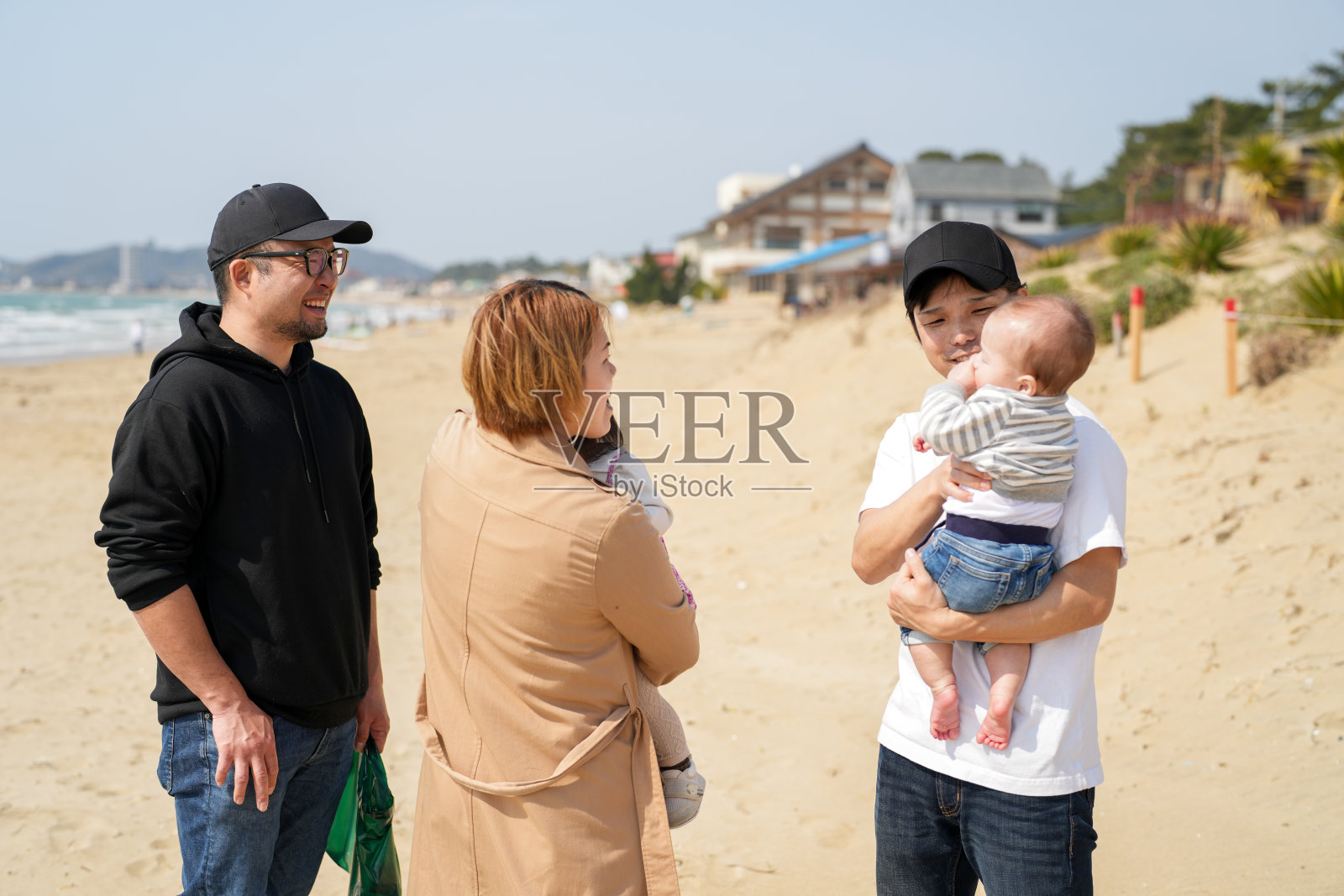 三月初，日本家庭一起享受海滩时光：一个六个月大的婴儿，一个一岁的小女孩，一个三岁的小女孩，以及三十多岁的父母。温暖而快乐的春季场景。照片摄影图片