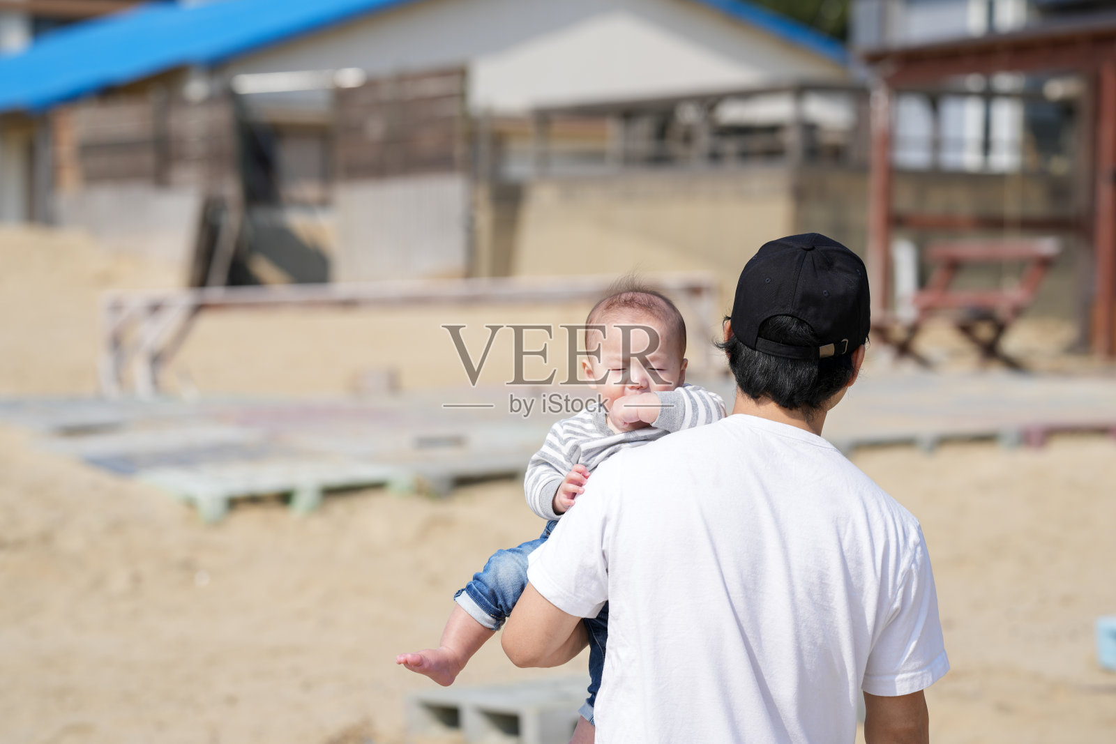 三月初，一位30多岁的日本父亲在海边的沙滩上背着他6个月大的宝宝，温暖的春季场景充满了家庭、快乐和亲密感。照片摄影图片