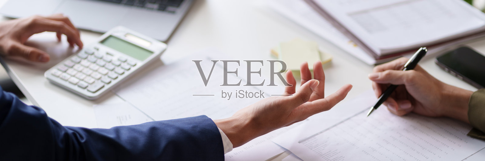 两个人在桌子旁进行讨论，重点关注他们的手和一份文件。背景中可见一台显示图表和数据的笔记本电脑。照片摄影图片