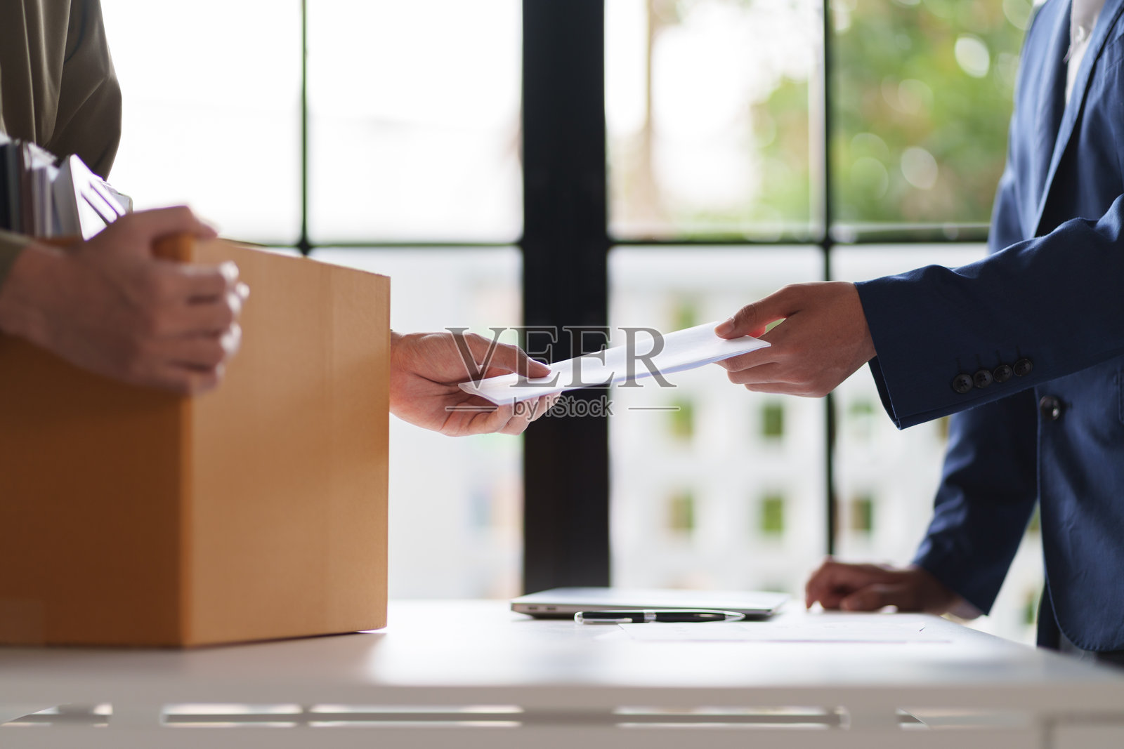 两个人在桌子上交换文件。一个人手里拿着一个装满办公用品的盒子，暗示可能的工作变动或项目交接。照片摄影图片