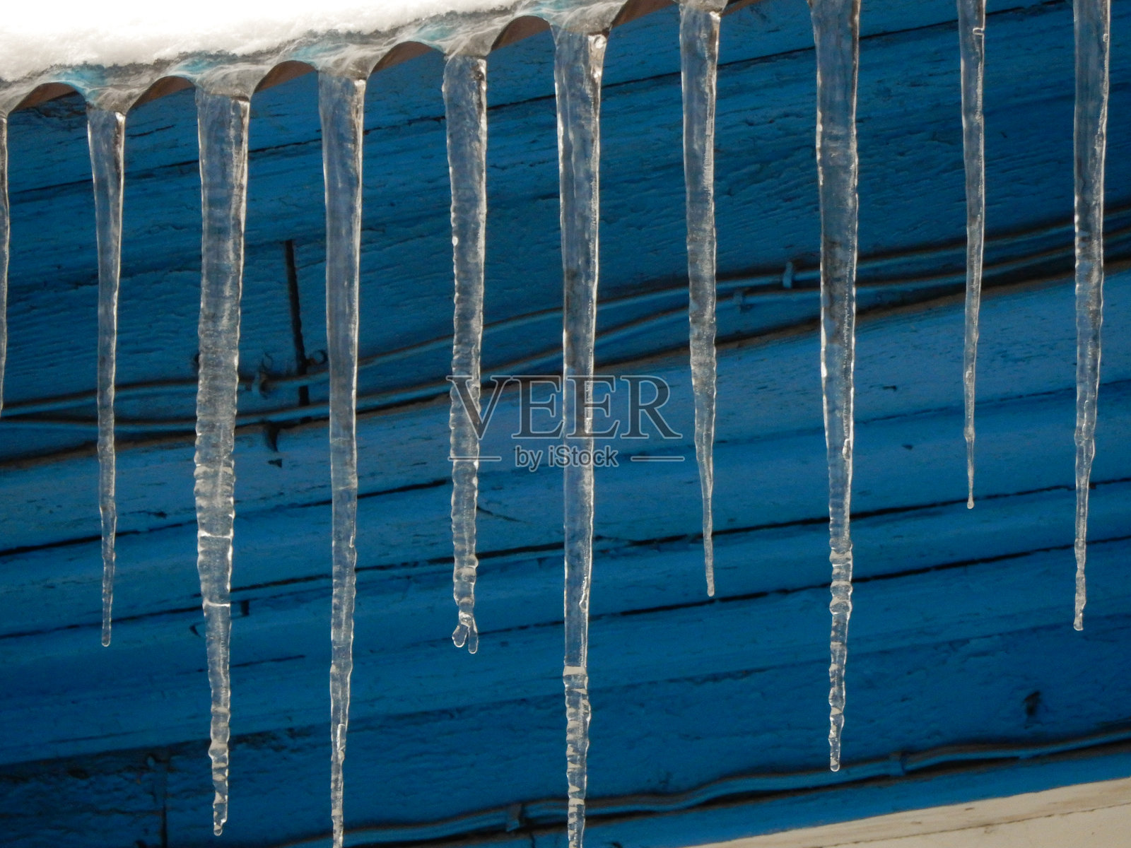 冰冷的冰柱悬挂在哈萨克斯坦阿拉木图的蓝色屋檐下照片摄影图片