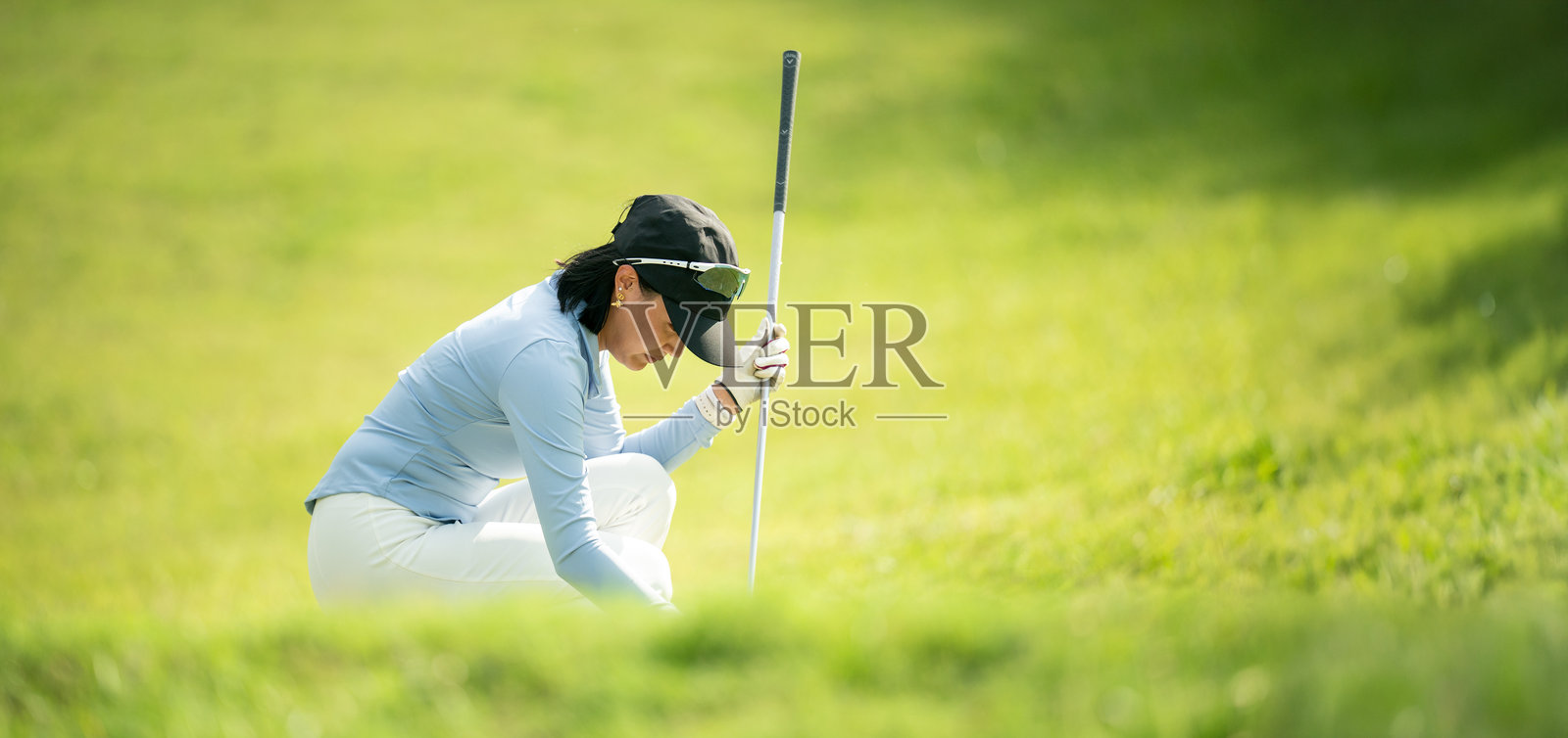 一位女性跪在草地上，手中握着一根高尔夫球杆。照片摄影图片