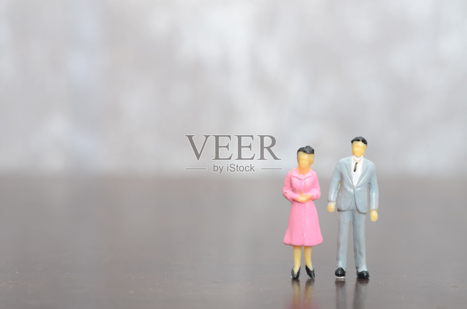 身穿灰色西装的小人和穿着粉色裙子的女性雕像，代表着一对专业搭档照片摄影图片