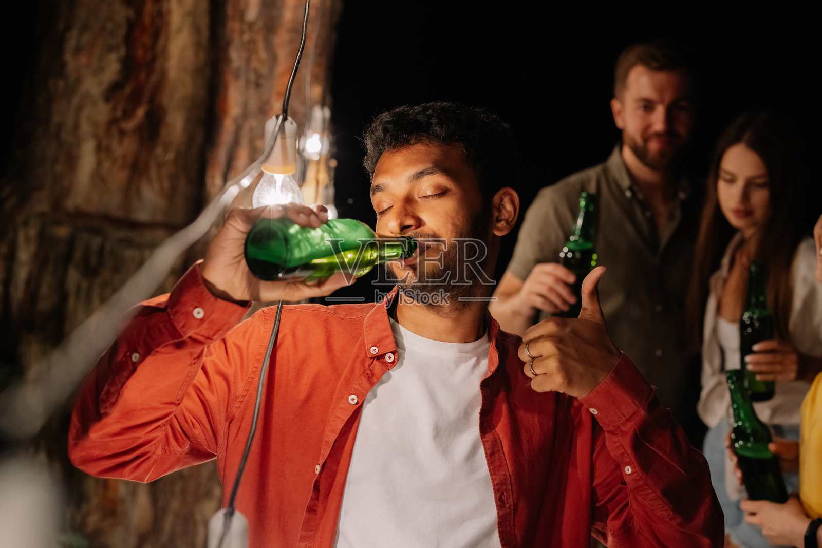 年轻男子在派对上喝啤酒并竖起大拇指。照片摄影图片