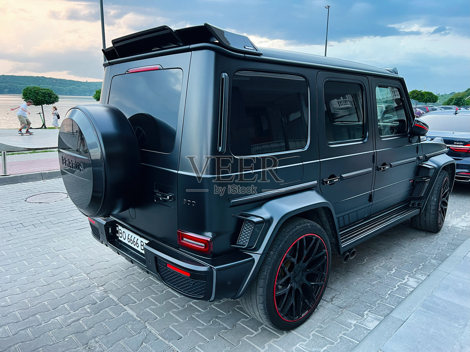 黑色豪华梅赛德斯-奔驰G级Brabus G800 G-Tronic SUV，配有定制轮毂，停靠在阳光明媚的水边。照片摄影图片