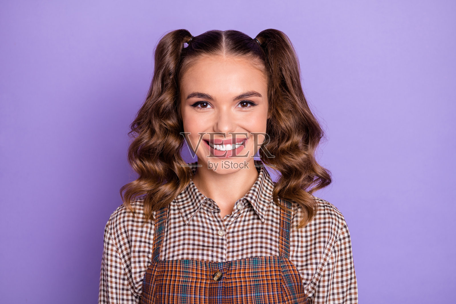 可爱的卷发小女孩灿烂微笑着看向镜头，背景为紫色。照片摄影图片