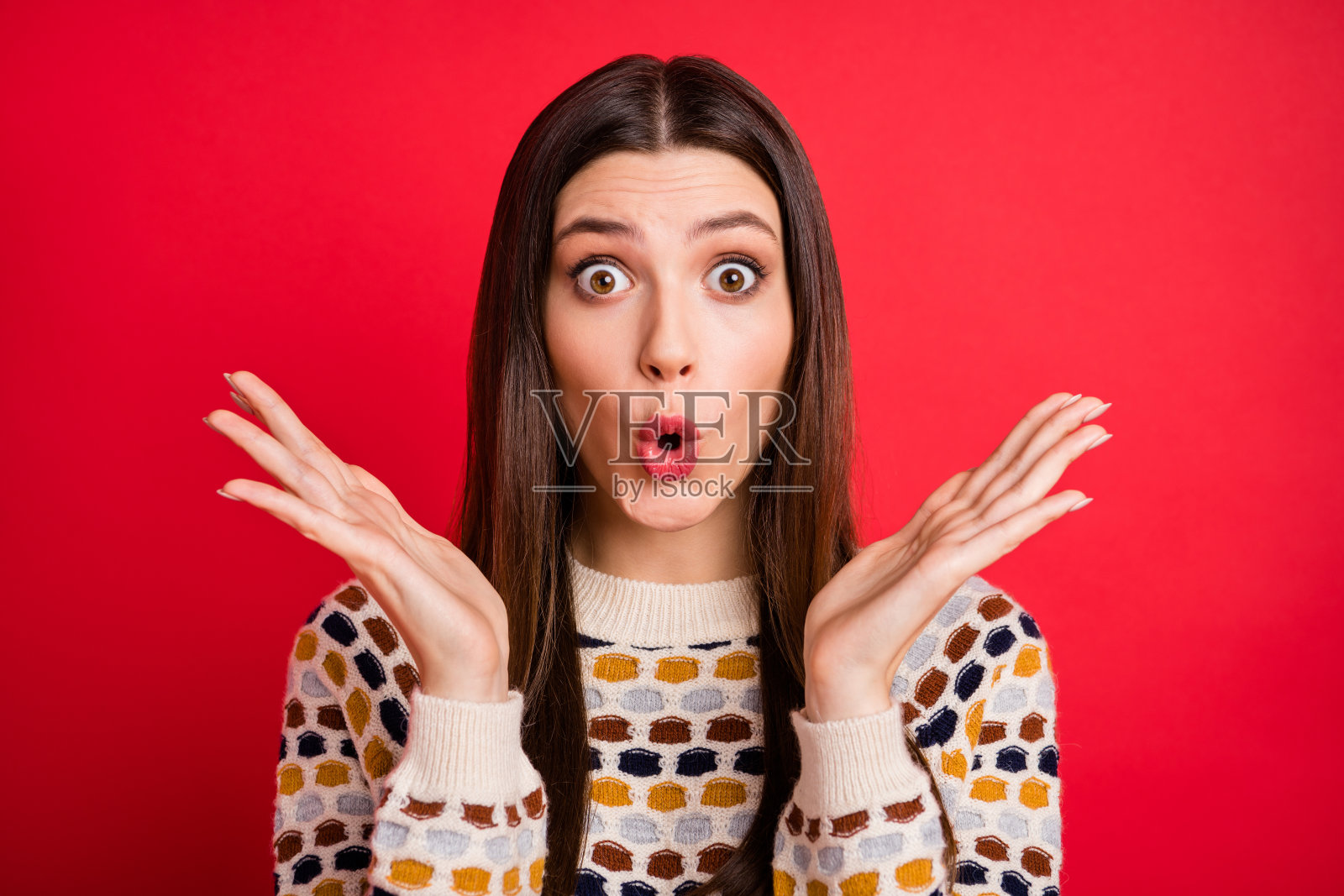 一个印象深刻的可爱女孩，双手举起，穿着五彩缤纷的毛衣，背景为红色。照片摄影图片