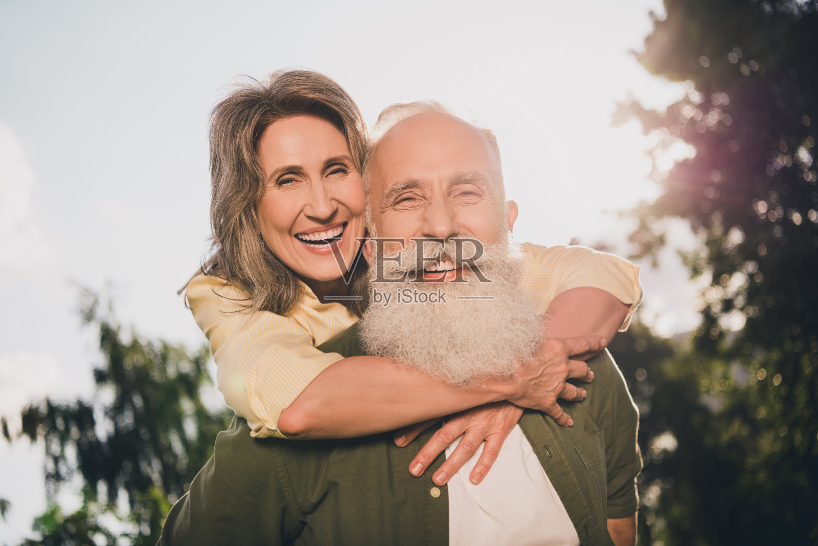 一对酷炫的退休白发夫妇在公园户外拥抱，背着对方，穿着休闲衬衫，庆祝周年纪念。照片摄影图片