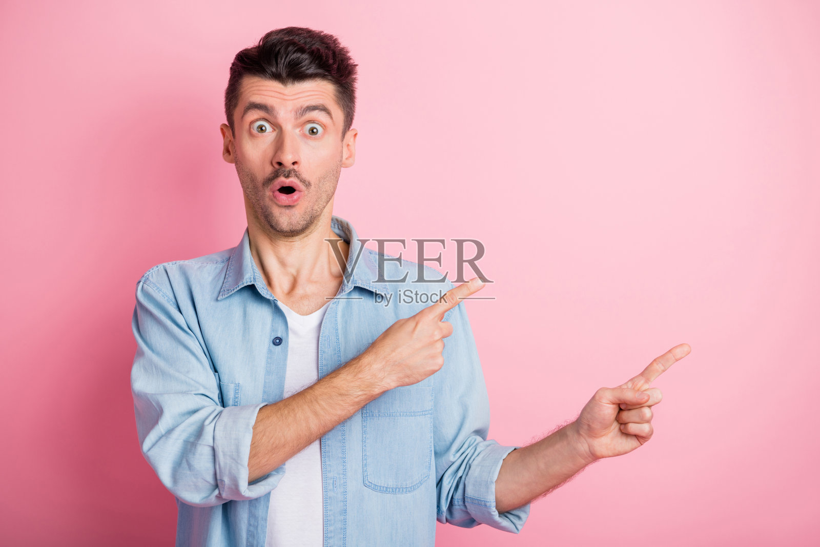 惊讶的学生在粉色背景前指着空白处，面露震惊之色的照片肖像照片摄影图片