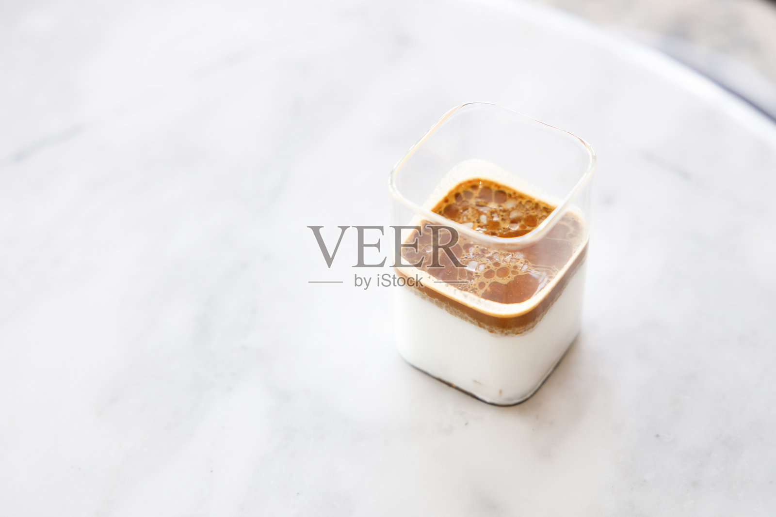 窗边白色大理石桌上的一杯牛奶脏咖啡。照片摄影图片