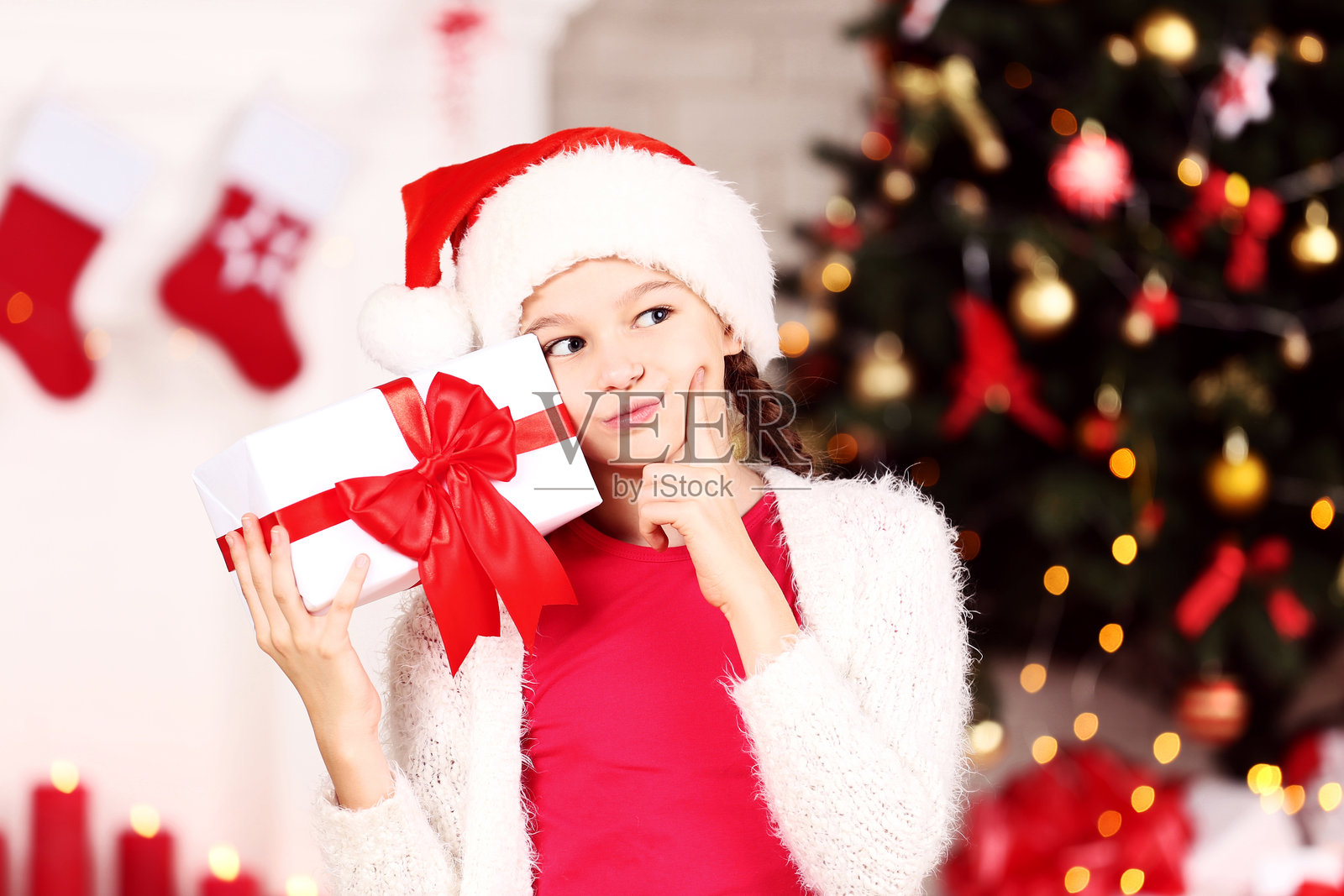 年轻女孩在家中圣诞树旁边与礼物盒子。照片摄影图片