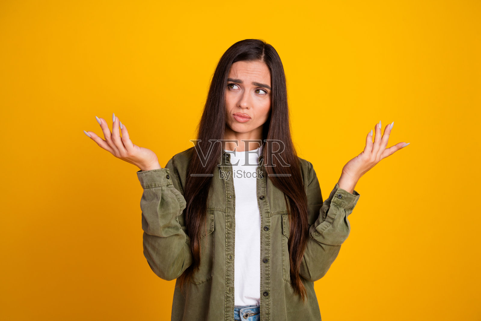 困惑的年轻女性在鲜艳的黄色背景前耸肩，穿着休闲服，表达不确定性照片摄影图片