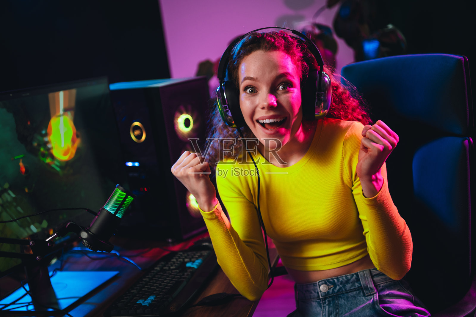 兴奋的游戏女孩在霓虹灯照亮的房间里享受视频游戏，展示现代家庭游戏设备。照片摄影图片