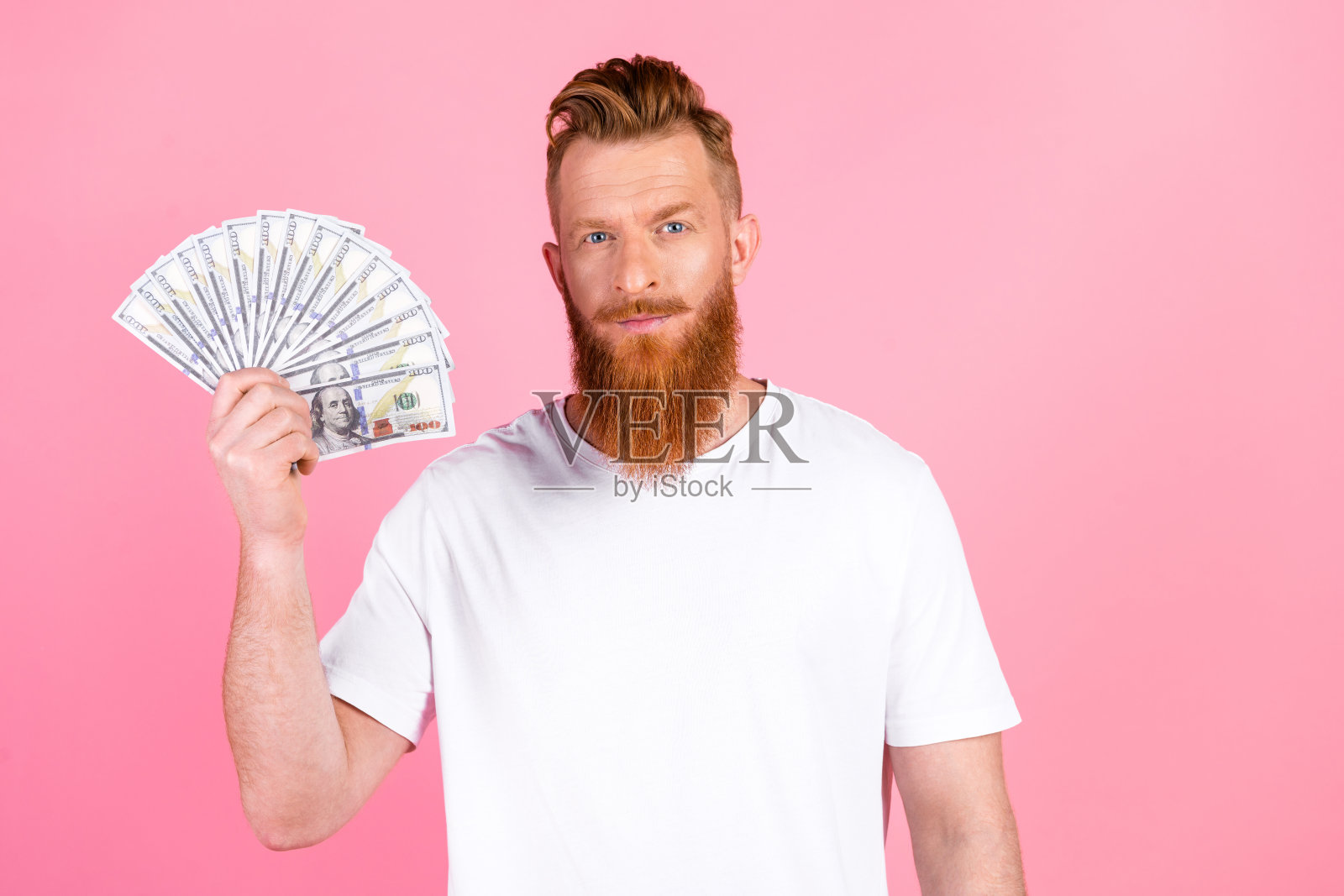 时尚的胡子男人在粉色背景前手持一叠美元，象征着财富与成功照片摄影图片