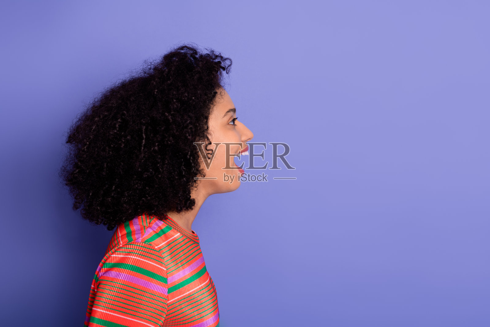年轻微笑女性的侧面轮廓，穿着鲜艳条纹衬衫，背景为紫色照片摄影图片