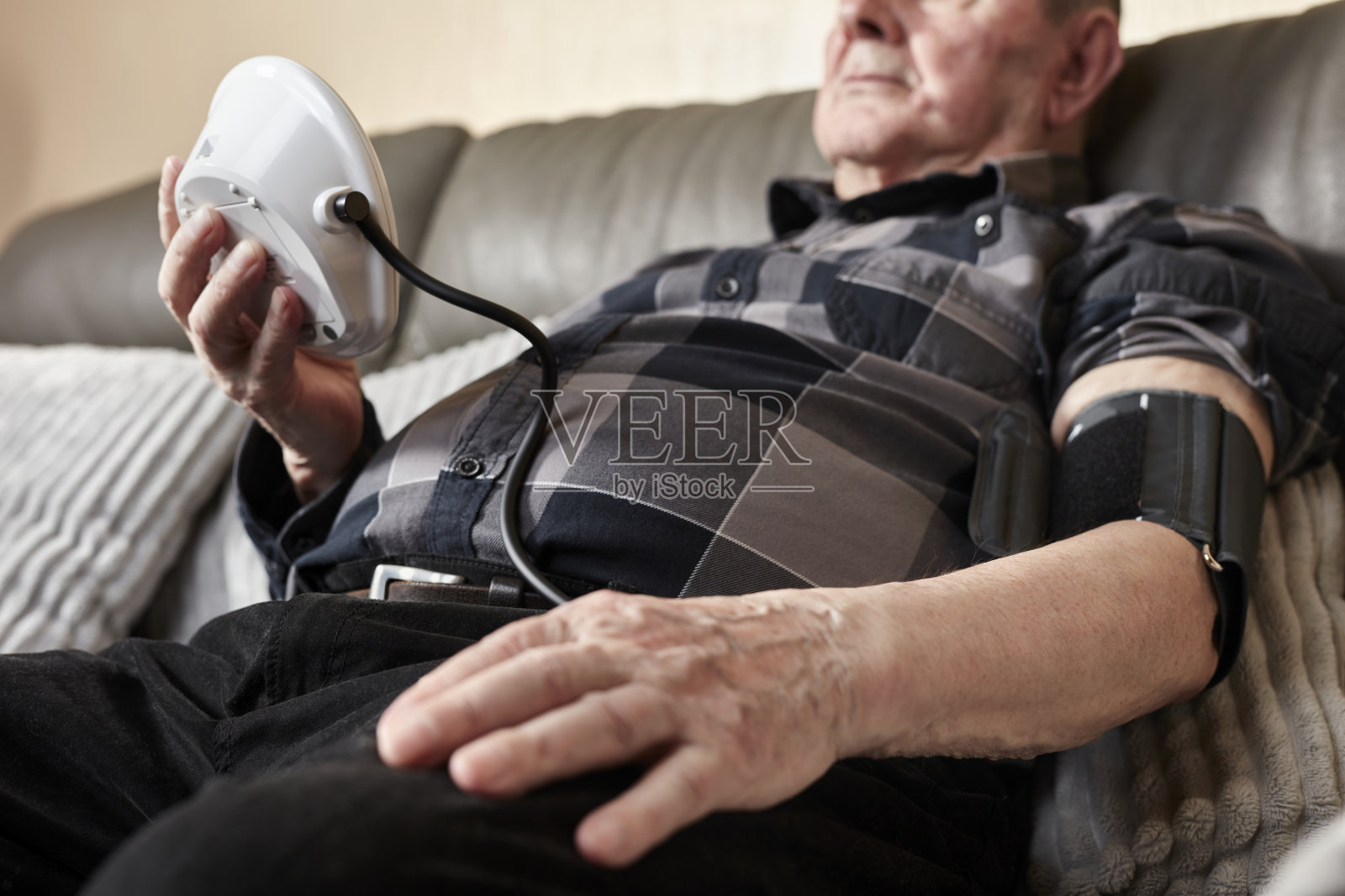 一位老年人坐在沙发上，使用家用血压监测仪，手放在腿上。照片摄影图片