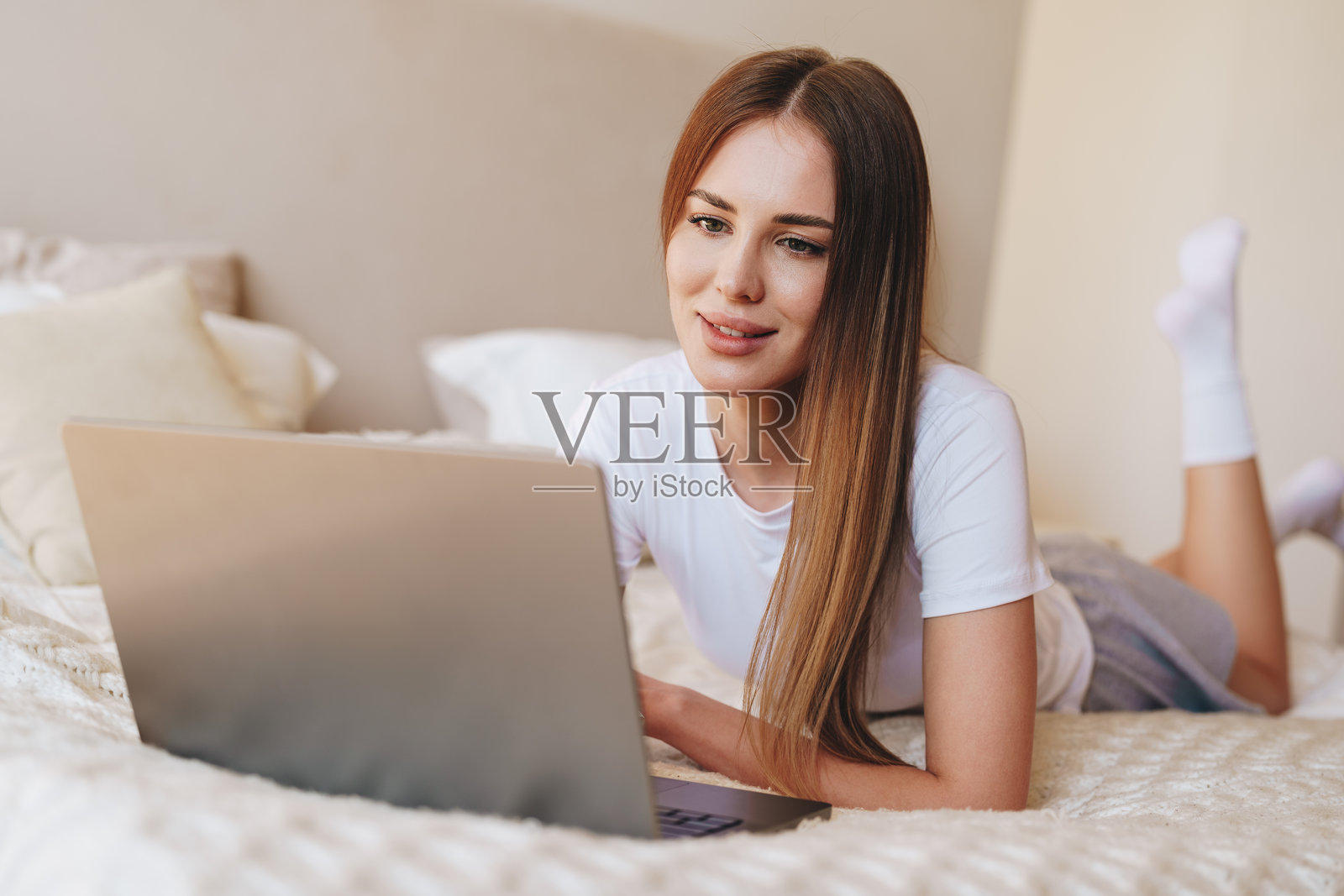 年轻女性在舒适的卧室环境中躺在床上放松并使用笔记本电脑工作照片摄影图片