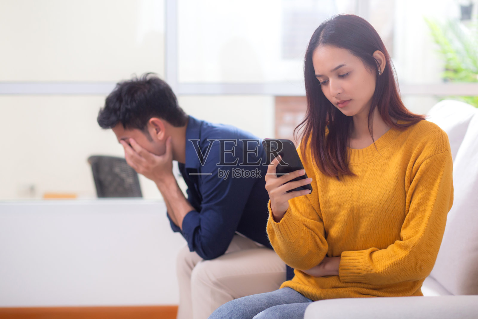 不快乐的亚洲夫妇坐在沙发上，面临家庭生活中的关系问题，情感冲突和疏离，夫妻之间感到沮丧和失望，互相忽视，表情困扰。照片摄影图片