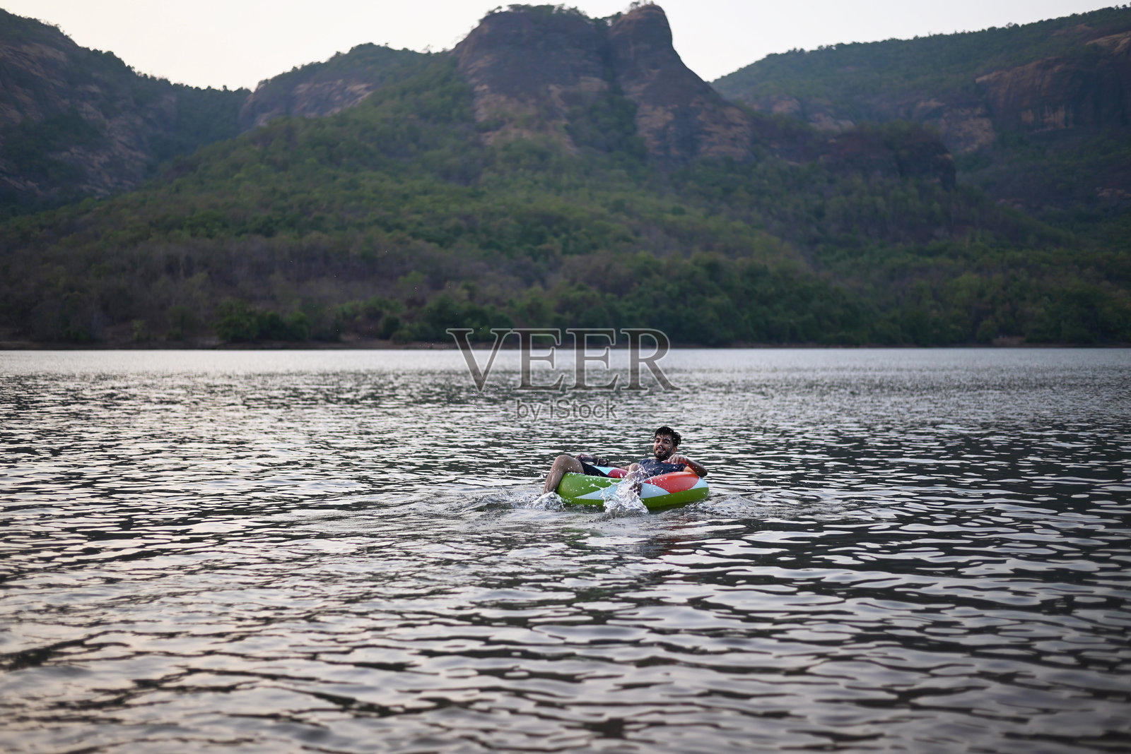 年轻男子在湖中日落时放松地坐在充气圈上照片摄影图片