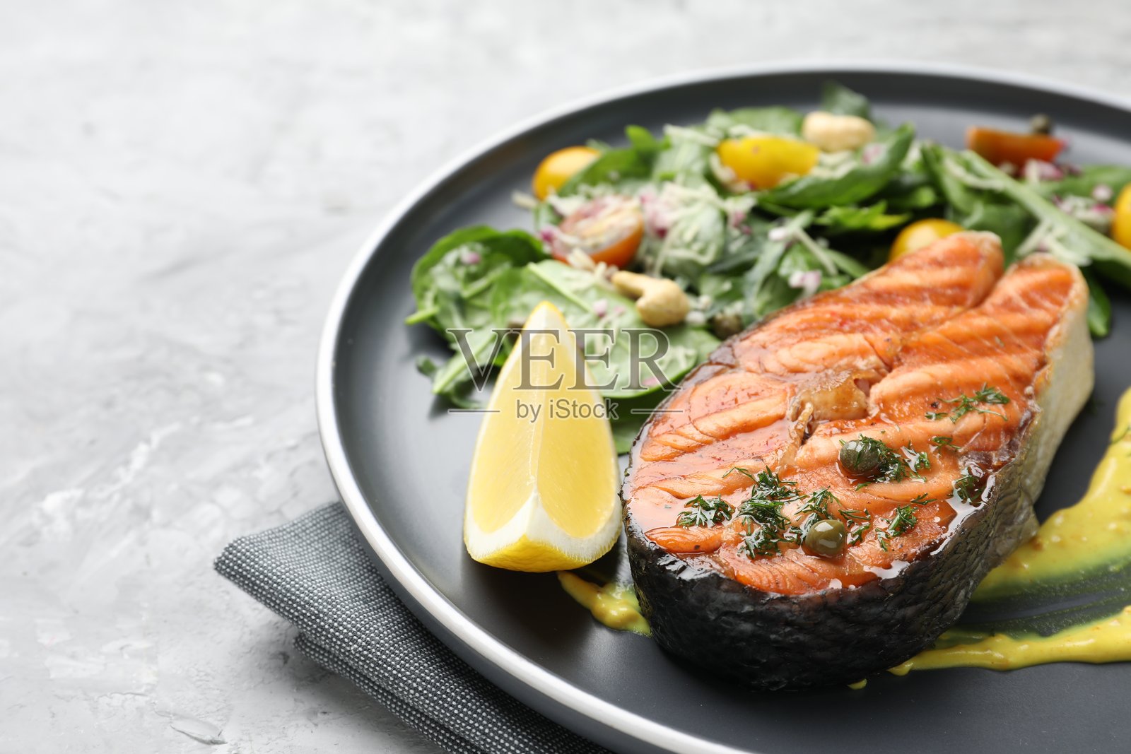 美味的烤三文鱼排配柠檬、酱汁和沙拉，放在灰色纹理桌面上，特写。留有文字空间。照片摄影图片