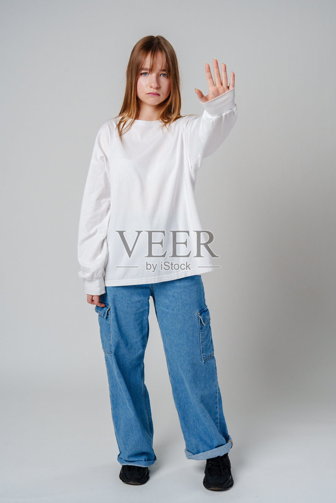 长发年轻女性在简单背景前举起手。照片摄影图片