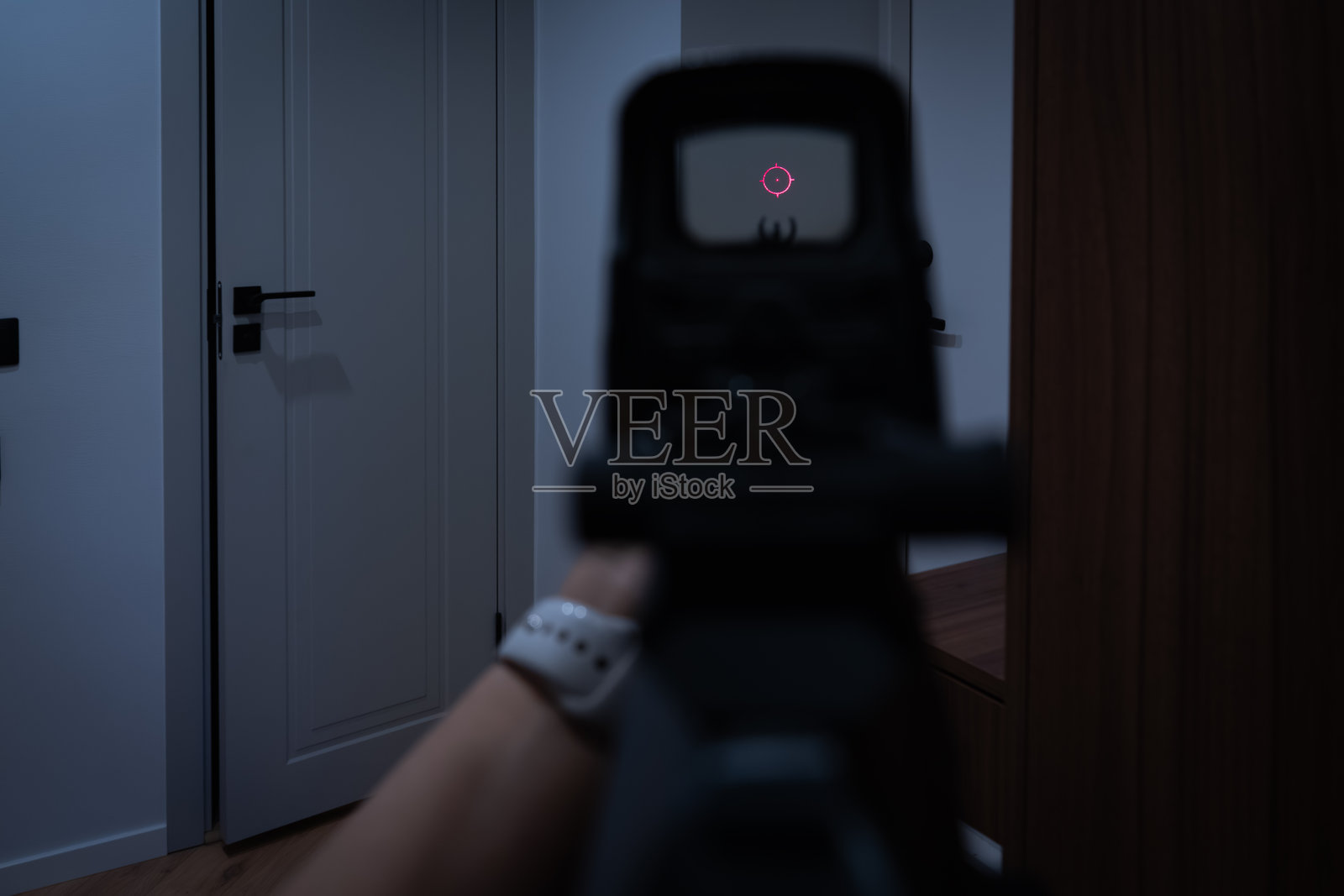 家庭防御概念：第一人称视角的女性手持突击步枪，通过全息瞄准器瞄准黑暗房间中的一扇门。照片摄影图片
