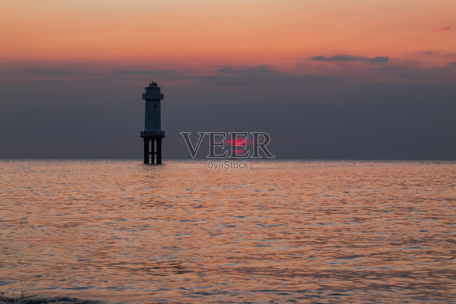 白色灯塔矗立在宁静的海面上，映衬着金色时光的日落。照片摄影图片