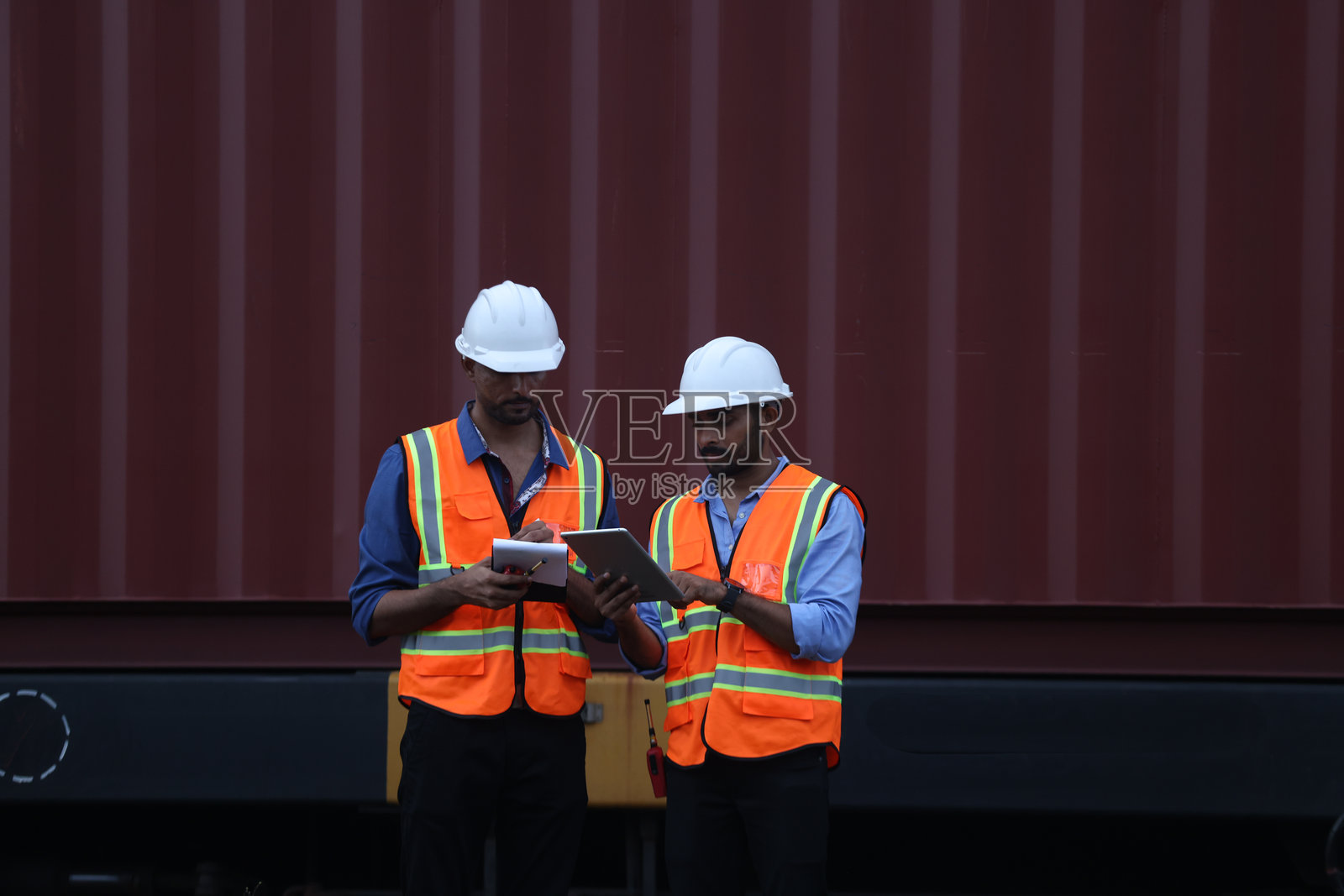 两名印度物流工作人员穿着安全夹克和个人防护装备，检查铁路运输中的集装箱，全球物流，集装箱货物通过铁路运输，物流经理和工作人员在铁路上检查集装箱。照片摄影图片