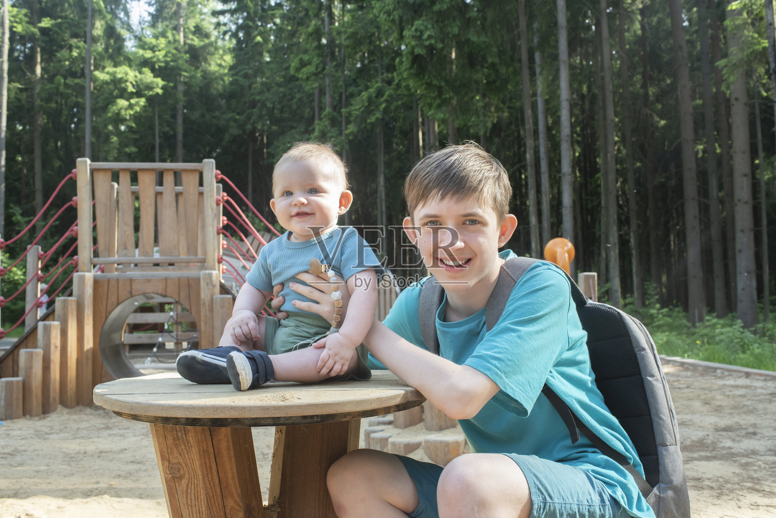 夏天，5个月大的男婴与12岁的哥哥在公园的游乐场玩耍。照片摄影图片