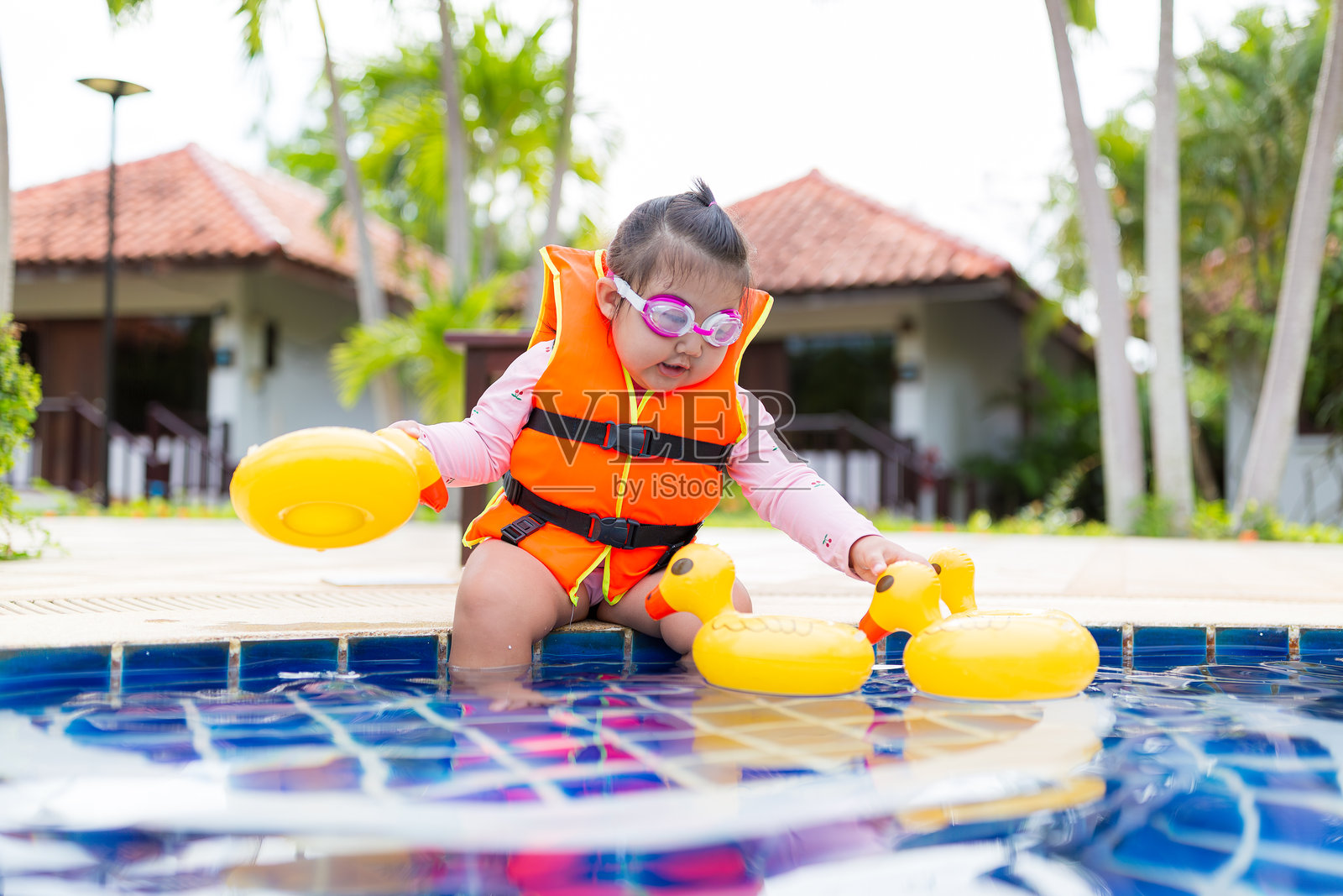 可爱的小女孩穿着救生衣在游泳池里玩耍，穿着救生衣的女孩坐在泳池边缘，玩水，夏季休闲活动。照片摄影图片
