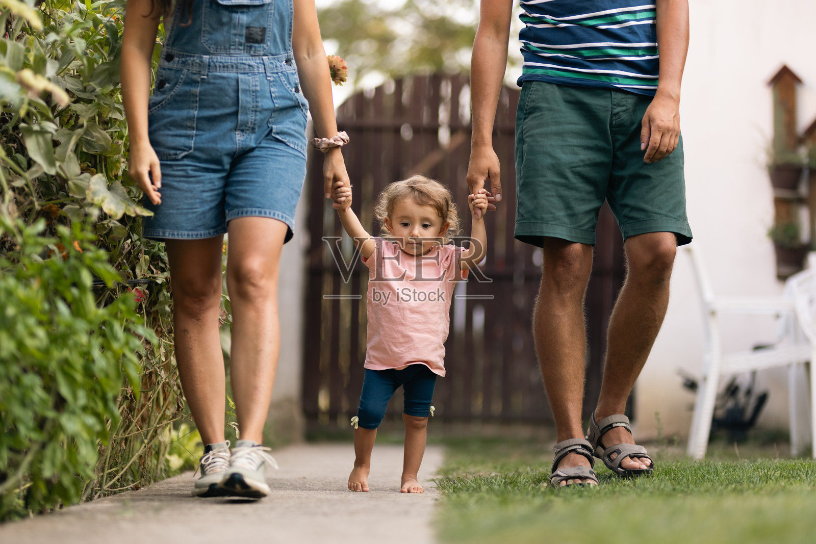 年轻父母在阳光明媚的日子里帮助他们的幼儿迈出第一步照片摄影图片