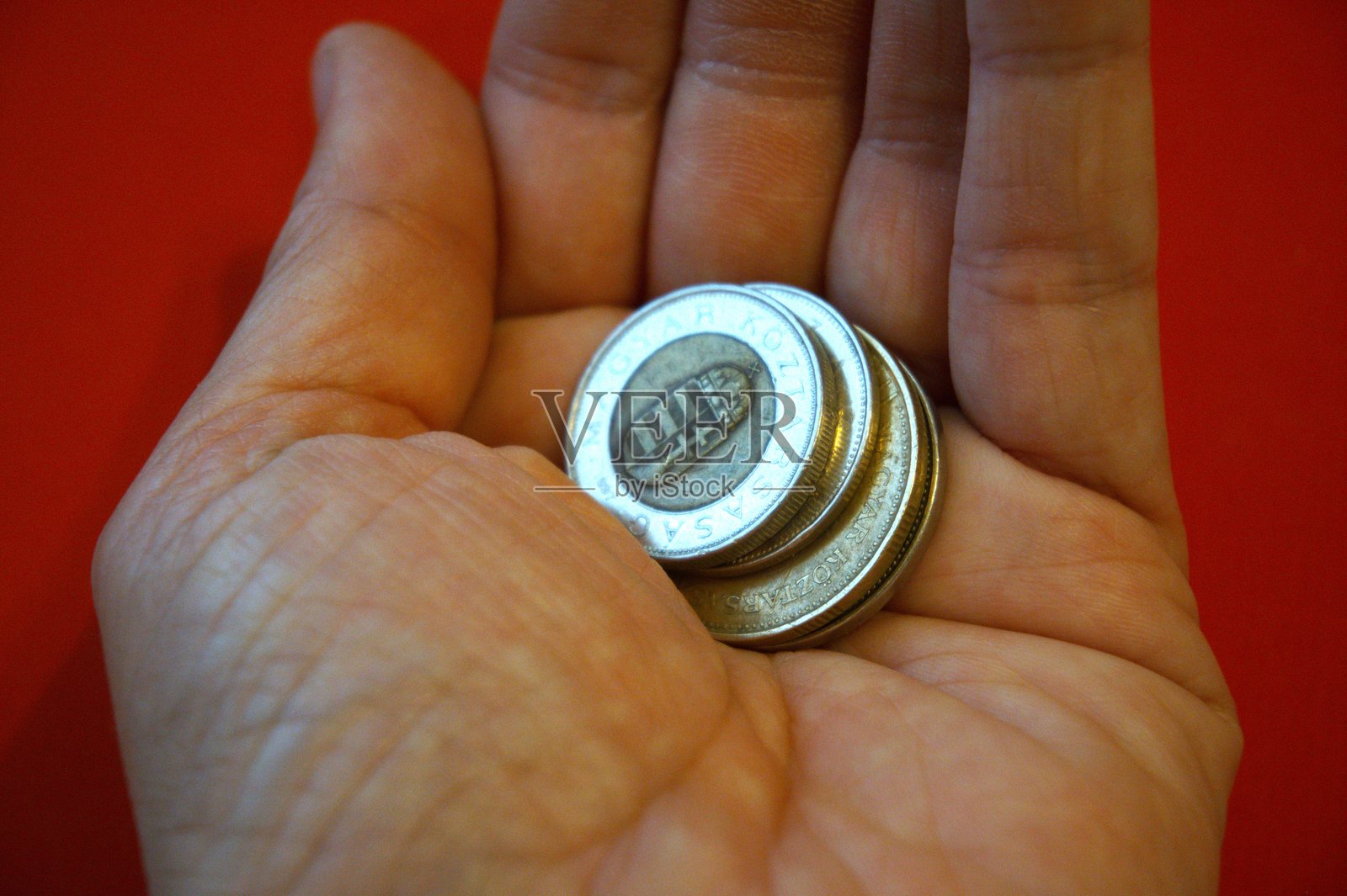 手中握着匈牙利福林硬币，背景为红色。照片摄影图片