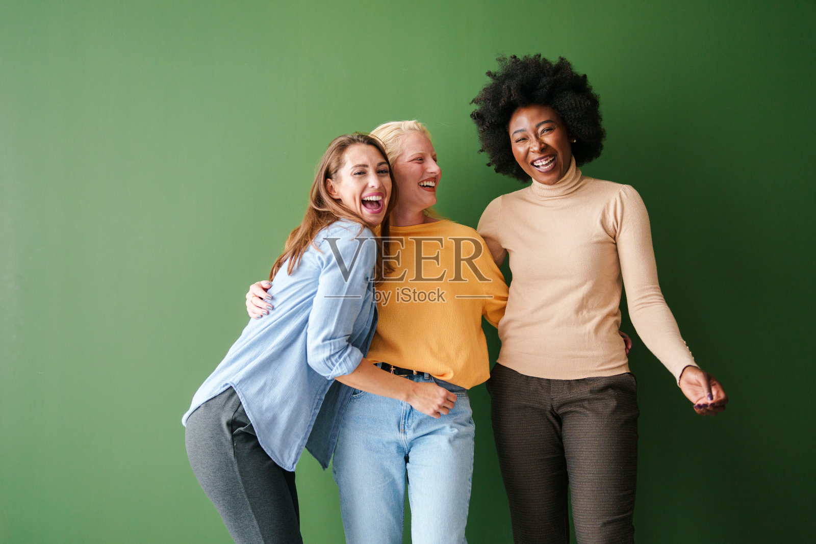 三位不同背景的朋友在自然光下，欢笑着，背景是生机勃勃的绿色工作室。照片摄影图片